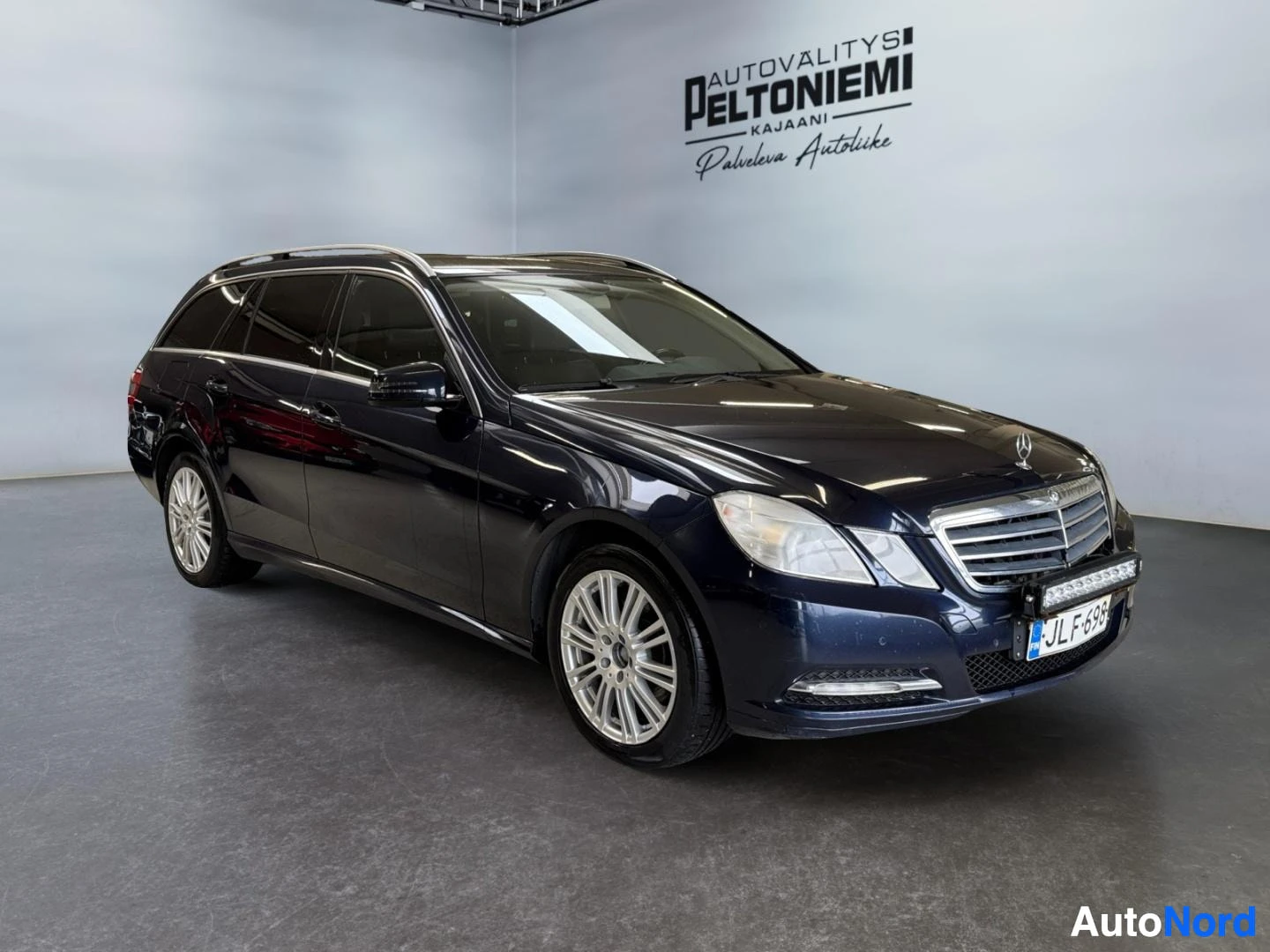 Etuviisto, nokka oikealle: Mercedes-Benzfarmari kolmasosakulmassa edestä vasemmalta, tummansininen korimalli studiosta.