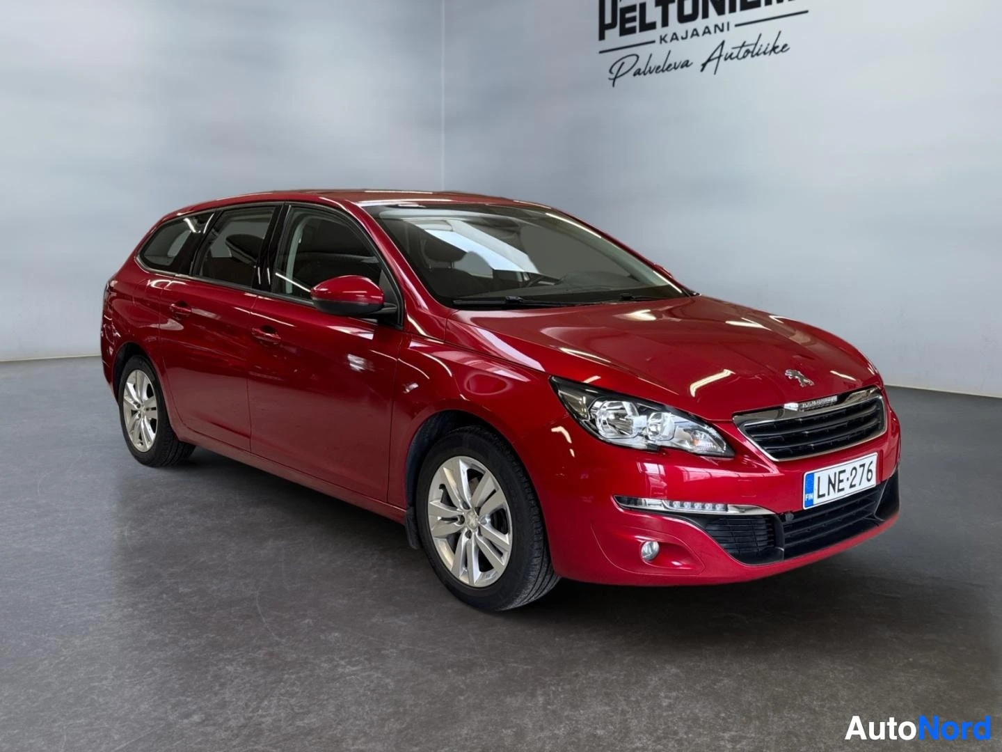 Etuviisto, nokka oikealle: Punainen Peugeot 308 SW farmari kulmasta edestäpäin kuvattuna näyttämössä.