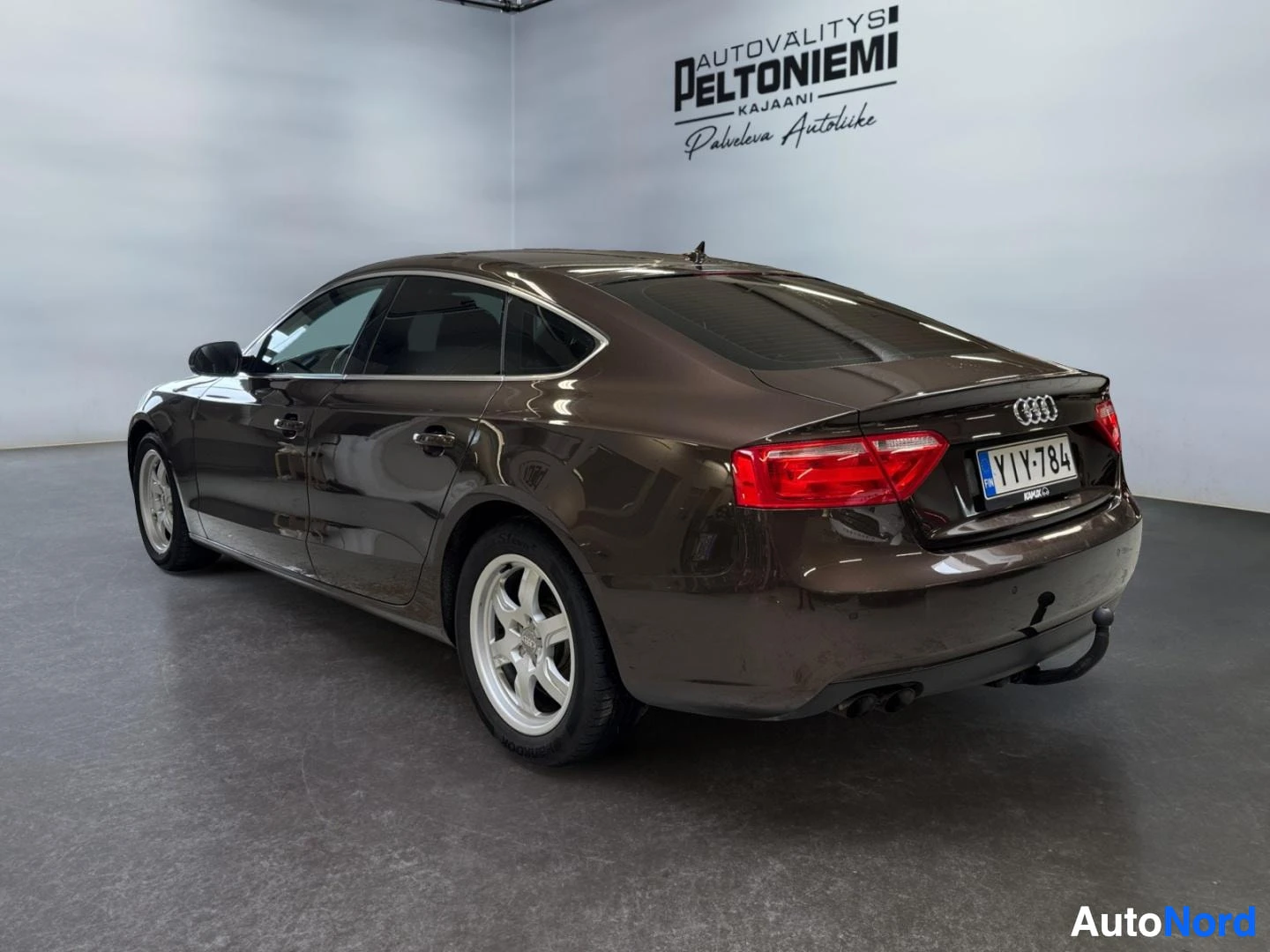 Takaviisto: Audi A5 Sportback, takakulma vasemmalta, tummanruskea sedan/korimalli rekisterikilpi, punaiset takavalot ja neljä pakoputkea näkyvissä.