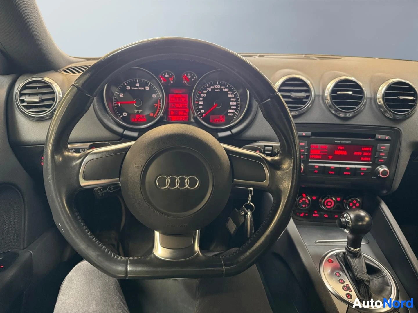 Ohjaamo: Audi TT:n ratissa ja kojelaudassa, automaattivaihteen valitsin ja Audi concert -radio näkyvät.