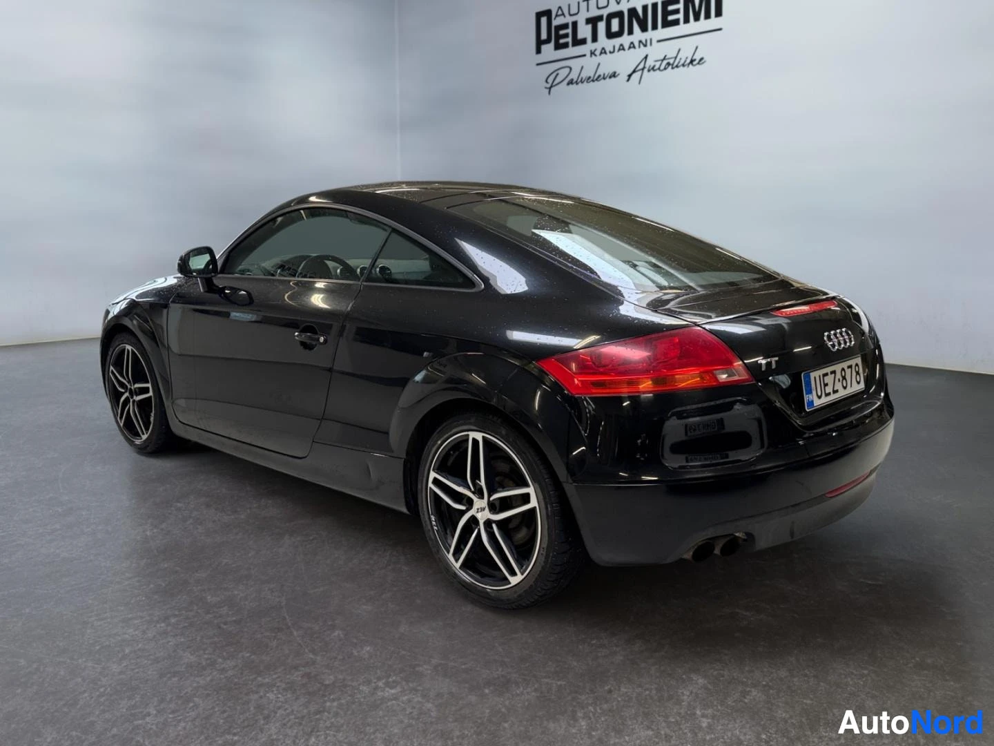 Takaviisto: Mustan Audi TT Coupén takakolmannesvaaka, rekisterikilpi ja kahdeksanpalkkiset kevytmetallivanteet näkyvät sisätiloissa.