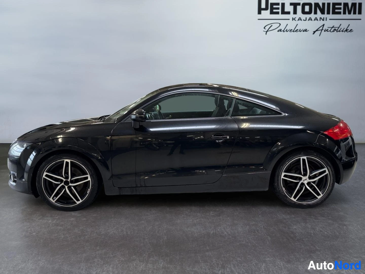 Sivulta: Mustan Audi TT Coupén sivukuva oikealta, kevytmetallivanteet ja kaksiovinen coupékori näkyvät sisätiloissa.