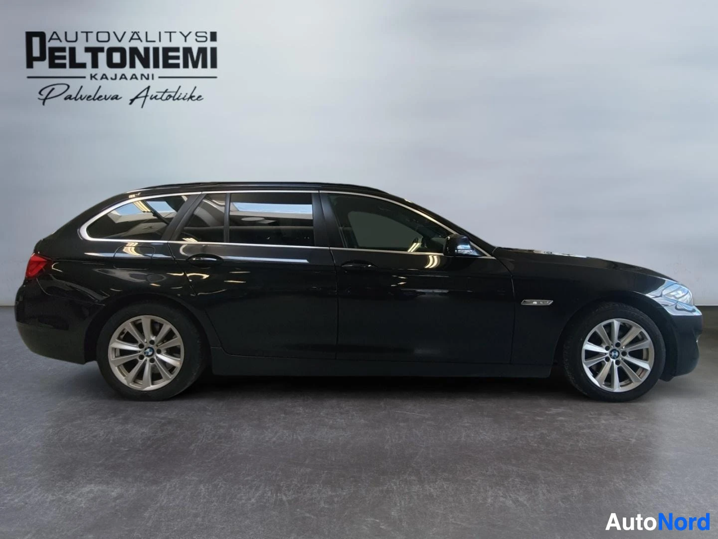 Sivulta: Musta BMW-farmari sivulta kuvattuna sisätiloissa.