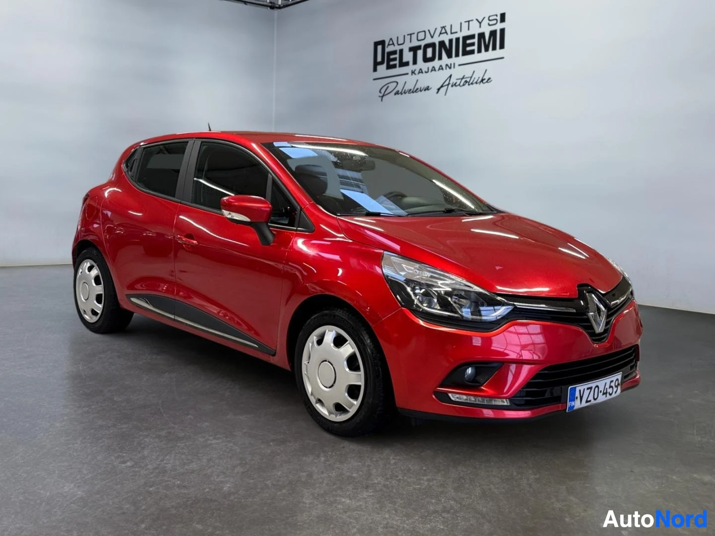 Etuviisto, nokka oikealle: Punainen Renault Clio -henkilöauto kuvattu edestä sivusuunnassa sisätiloissa.