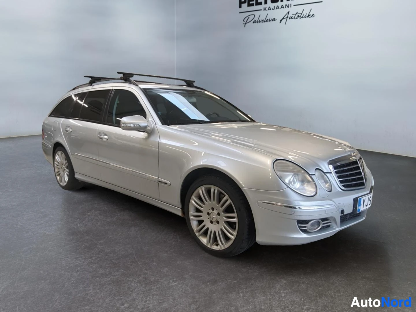 Etuviisto, nokka oikealle: Hopeanharmaa Mercedes-Benz E-sarjan farmari sisätiloissa, kolmen neljäsosan etunäkymä.