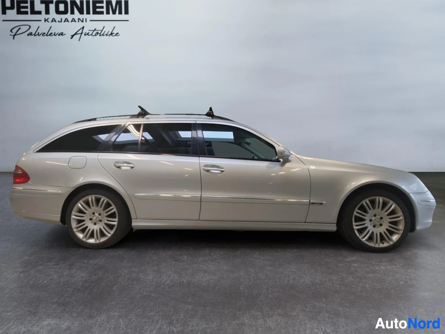Takaviisto: Hopeanharmaa Mercedes-Benz E-sarjan farmari sivulta takaa kuvattuna, kattokaiteet ja kevytmetallivanteet näkyvissä.