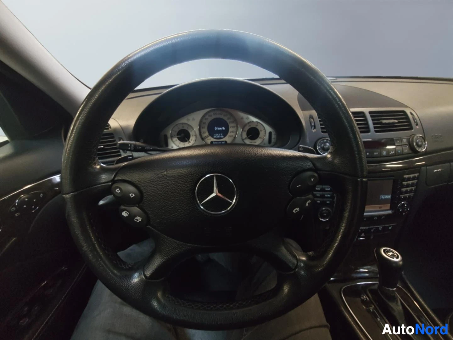 Muu: Ohjaamo näkyvissä Mercedes-tunnusmerkillä ohjauspyörässä; kojelaudan mittaristo näkyy pyörän takana, keskikonsolissa radio ja ilmastointiautomaatin säätimet.