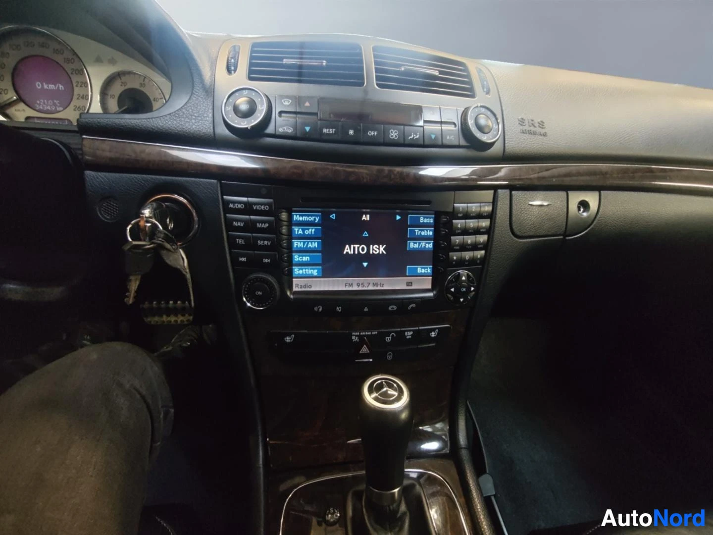 Muu: Keskikonsoli lähikuvassa: auton avaimet virtalukossa, radio/monitoiminäyttö, ilmastointiautomaatin säätimet ja Mercedes-merkkinen vaihteenvalitsimen nuppi.
