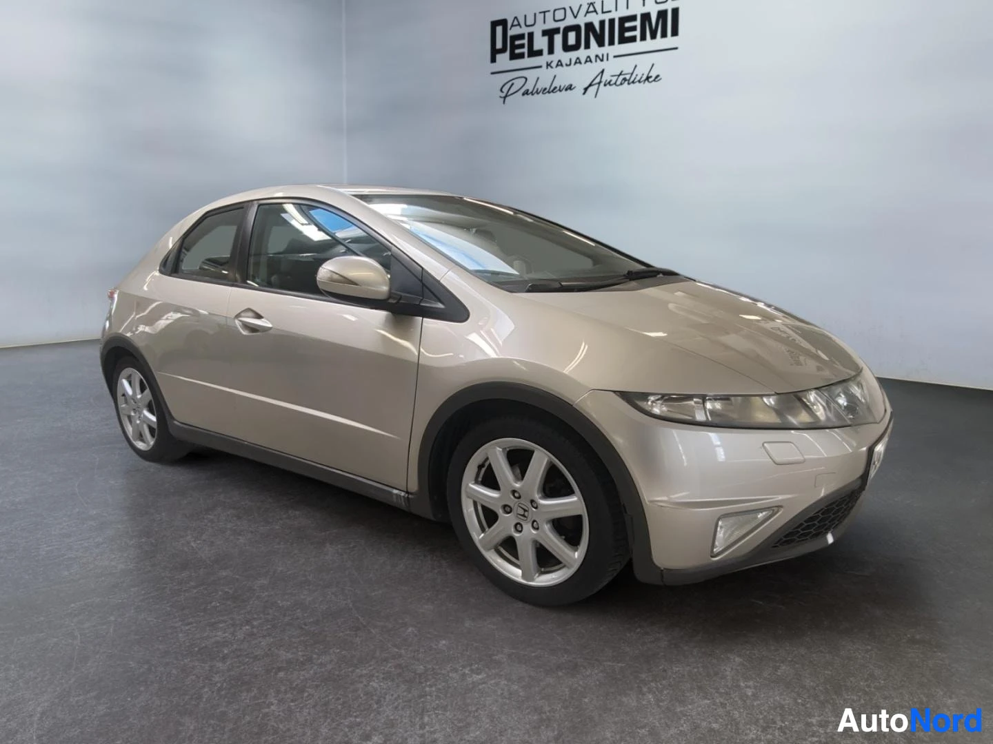 Etuviisto, nokka oikealle: Honda Civic -viistoperä beigeen sävytetynä kuvattuna edestä kolmannesnäkymässä sisätiloissa.