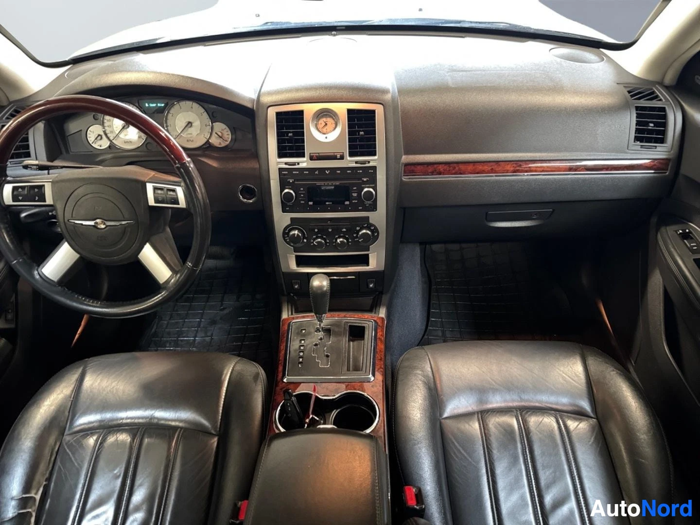 Muu: Ohjaamo Chrysler 300C:sta: tumma nahkasisusta, puusisäpaneelit, mittaristo ja keskikonsoli näkyvät.