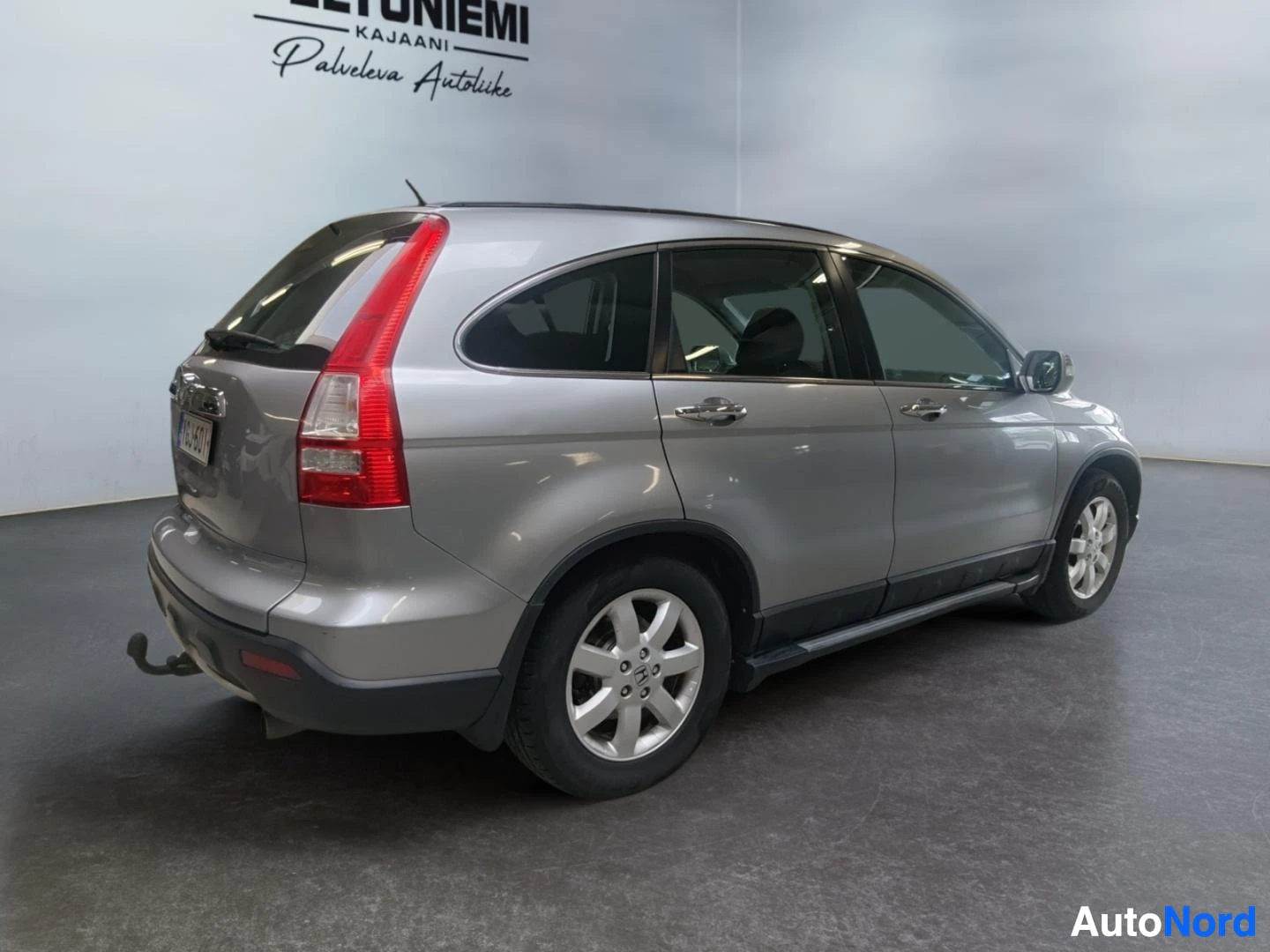 Takaviisto: Hopeanharmaa Honda CR-V takaa sivulta kuvattuna sisätiloissa, näkyvissä takavalot, perävaunukoukku ja kattokaiteet.