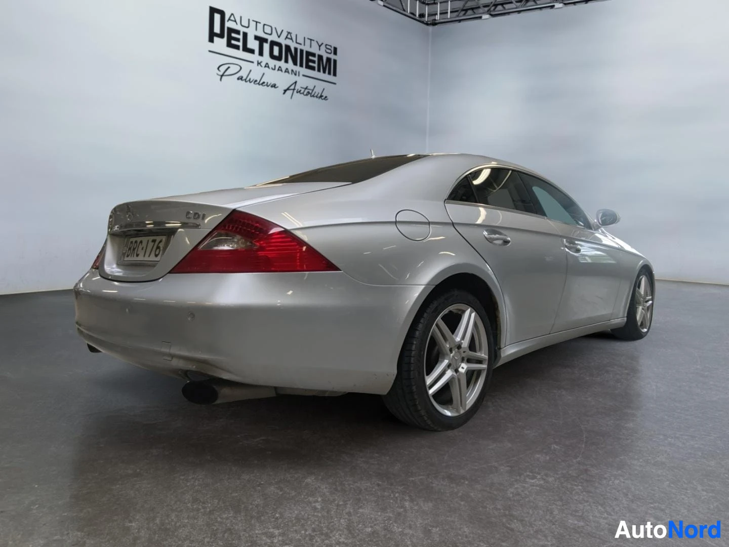 Takaviisto: Hopeinen Mercedes-Benz CLS -mallininen takaa oikealta sivulta kuvattuna sisätiloissa.