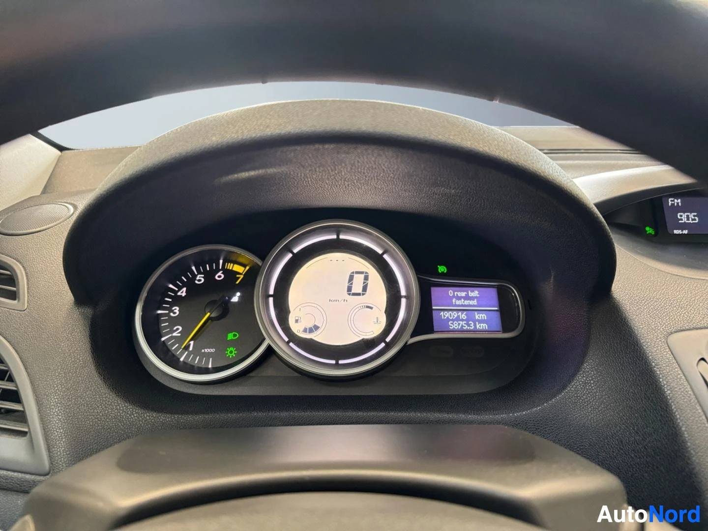 Edestä: Kojelaudan mittaristot lähikuvassa: nopeusmittari, keskellä digitaalinäyttö (0 km/h) ja文字n rivi '0 rear belt fastened', '190916 km', '5875.3 km'.