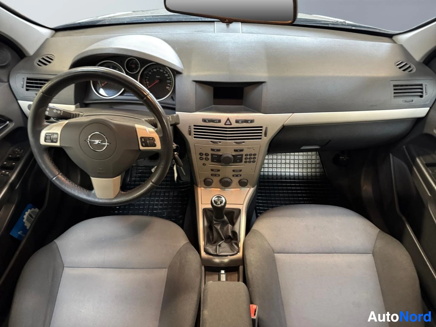 Muu: Opel Astran kojelauta ja ohjaamo ylhäältä kuvattuna; Opel-tunnuksellinen ohjauspyörä, analogiset mittarit, keskikonsolilla manuaalivaihteen keittiö ja radio/nah