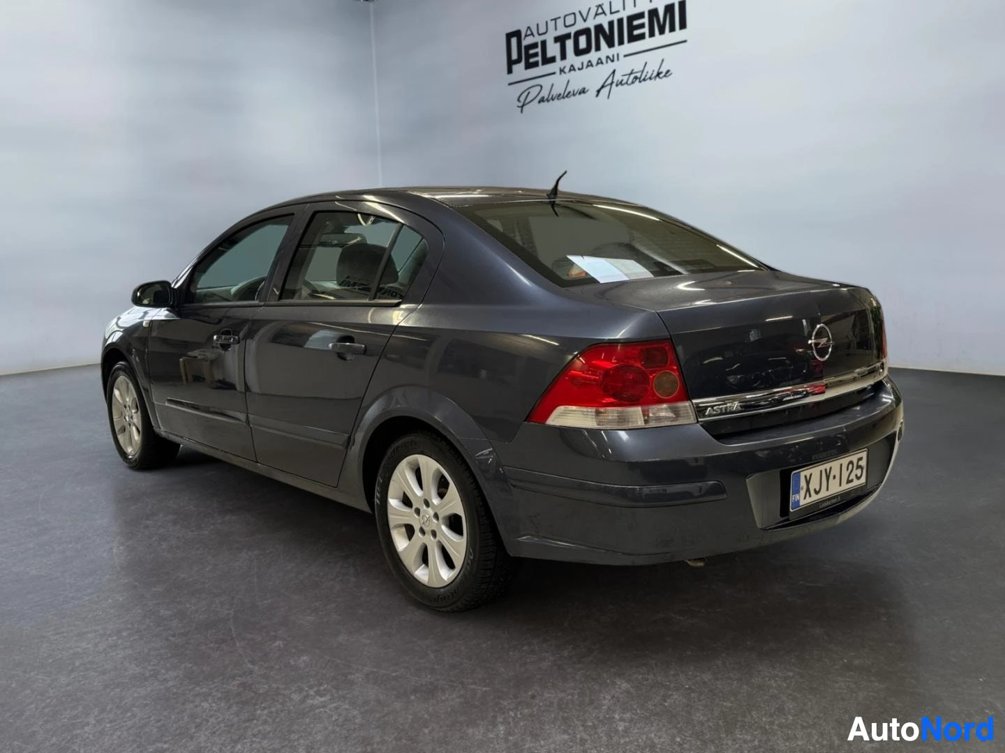 Takaviisto: Opel Astra -sedanin takakulma kuvattuna takaa vasemmalta, tummanharmaa koripelti ja rekisterikilpi näkyvät.