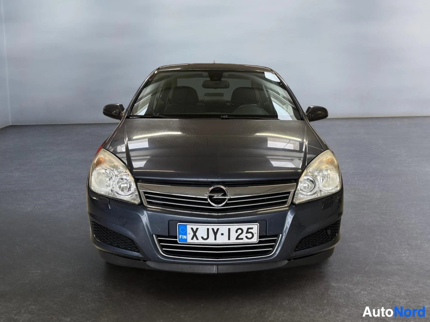 Edestä: Opel Astra -sedanin keulakuva suoraan edestä, tummanharmaa kori ja rekisterikilpi.