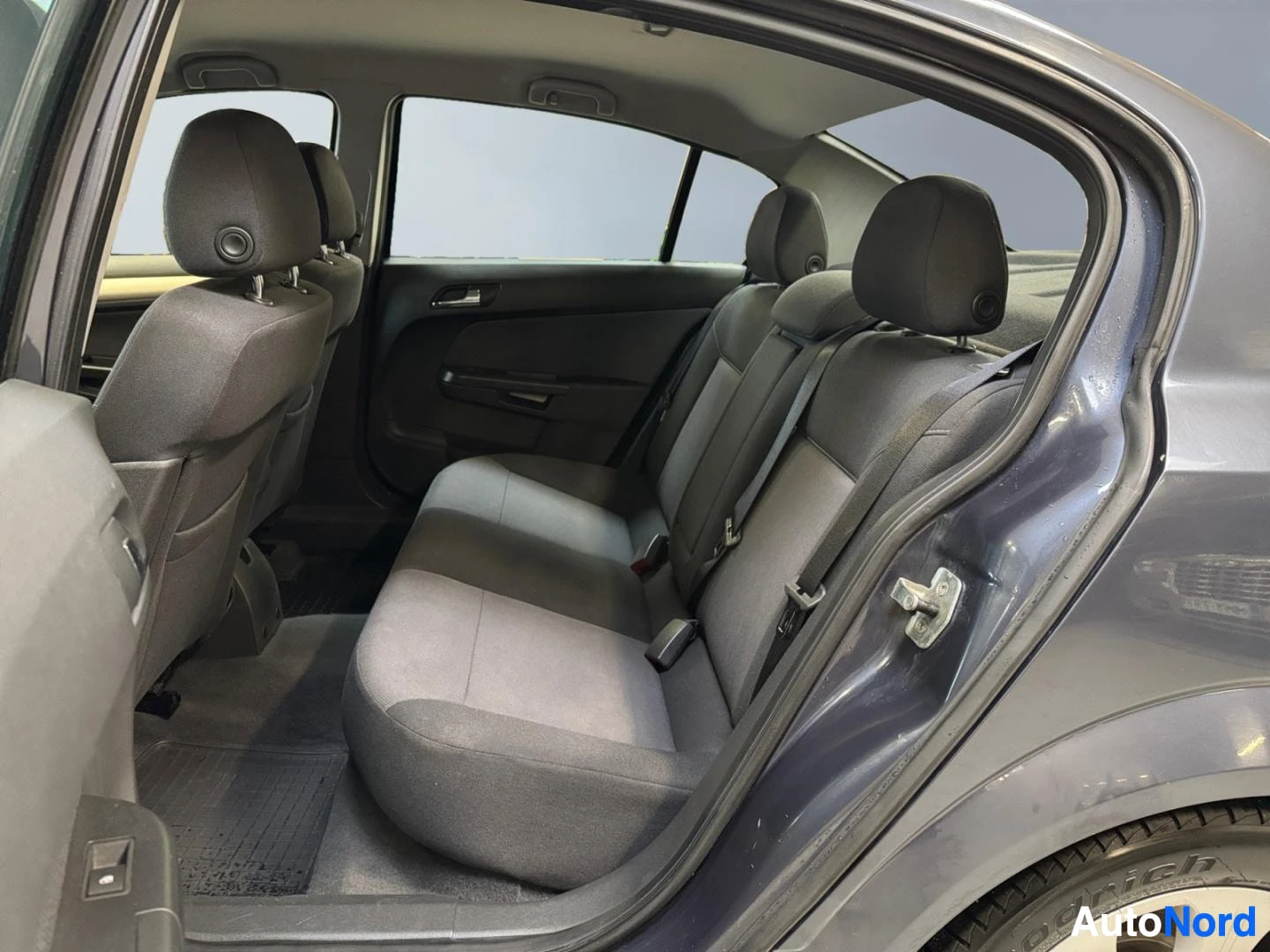 Muu: Opel Astran takapenkin sisätila takaovesta katsottuna; tummat kankaanverhoillut istuimet ja B-pylvään turvavyöt.