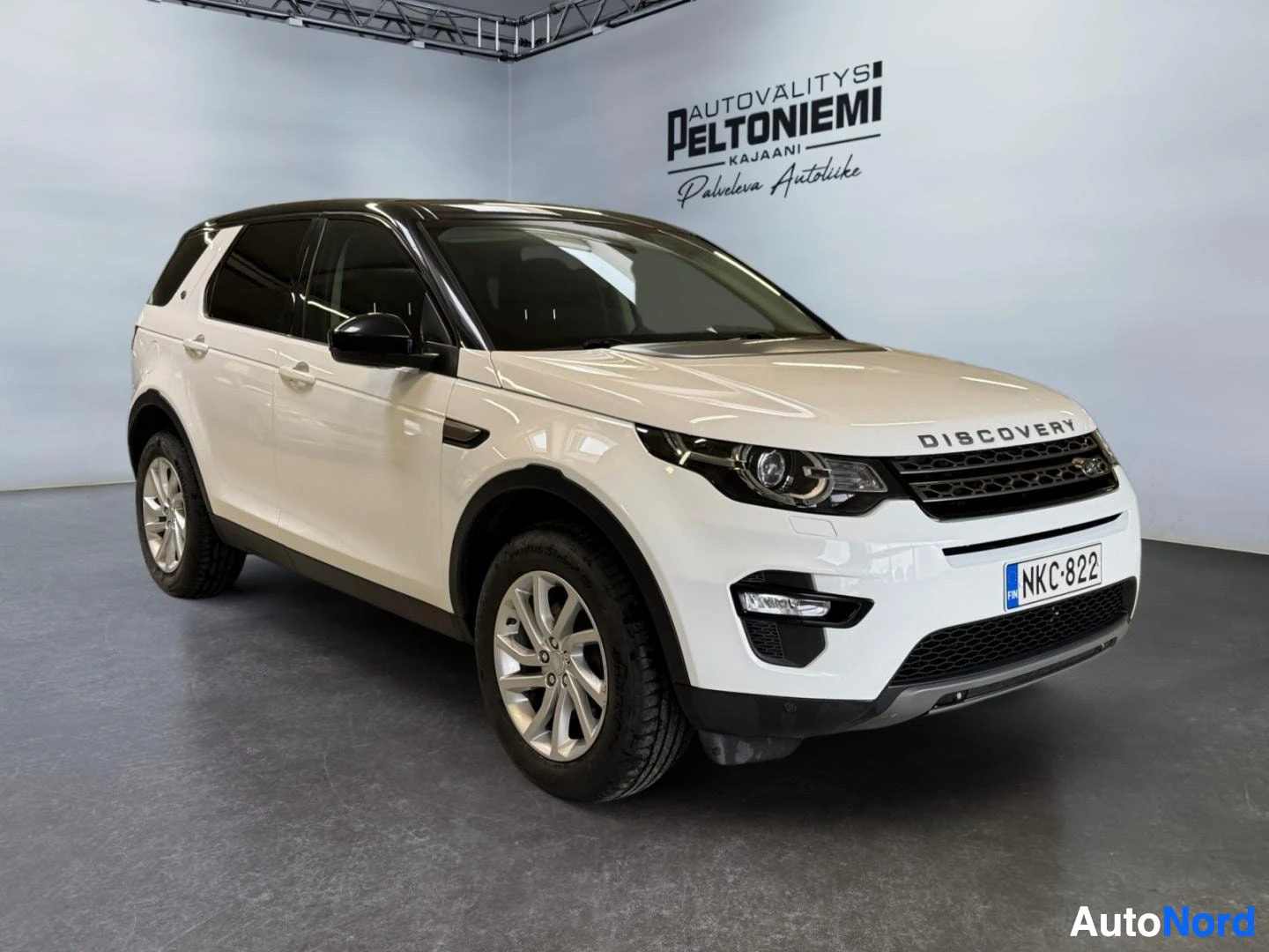 Etuviisto, nokka oikealle: Land Rover Discovery Sport etuviistokuva oikealta, valkoinen korimaalari ja musta katto, rekisterikilpi.