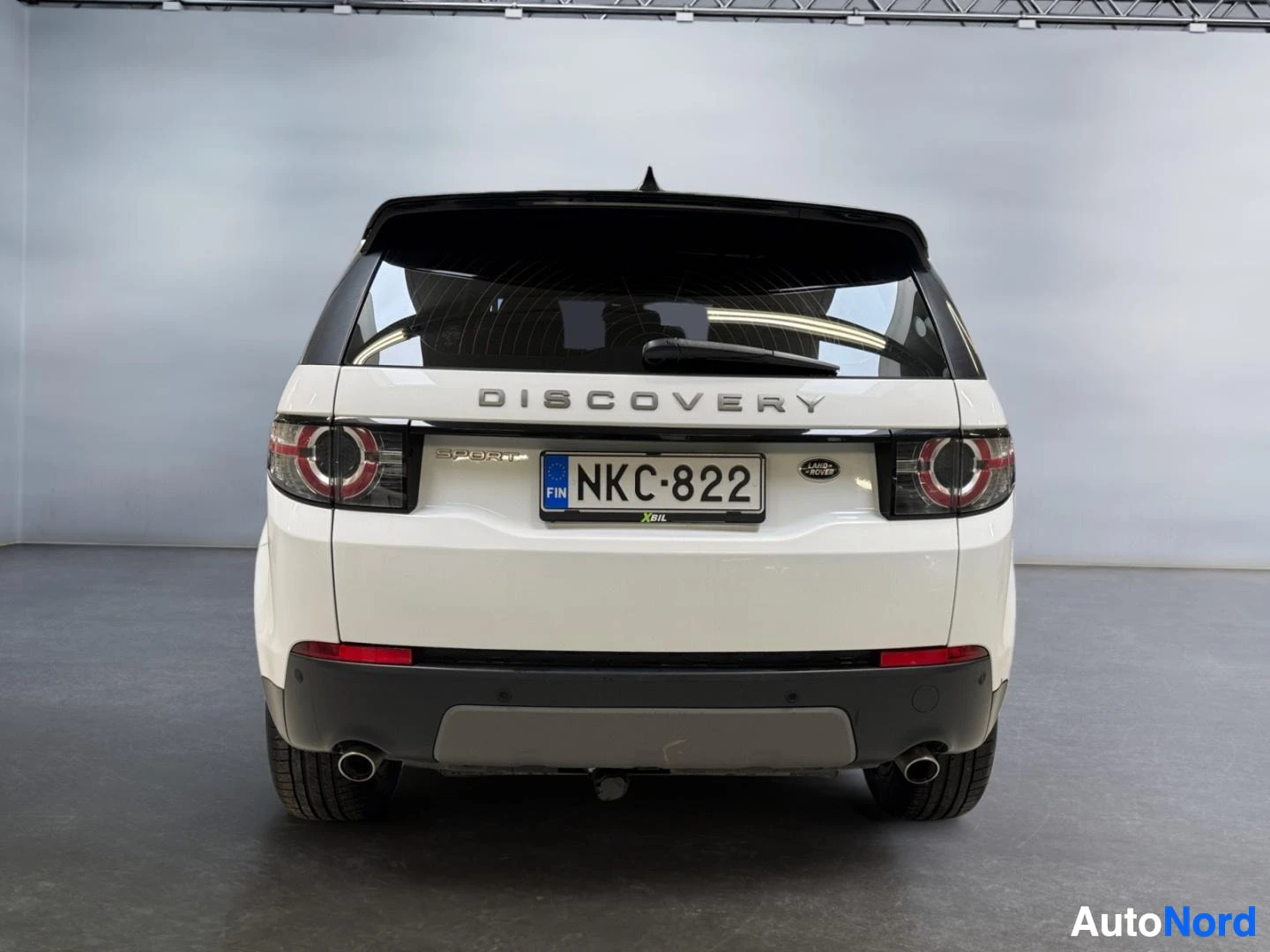 Takaa: Land Rover Discovery Sport suora takaa, valkoinen kori, DISCOVERY-teksti, kaksiosaiset pakoputket ja rekisterikilpi.