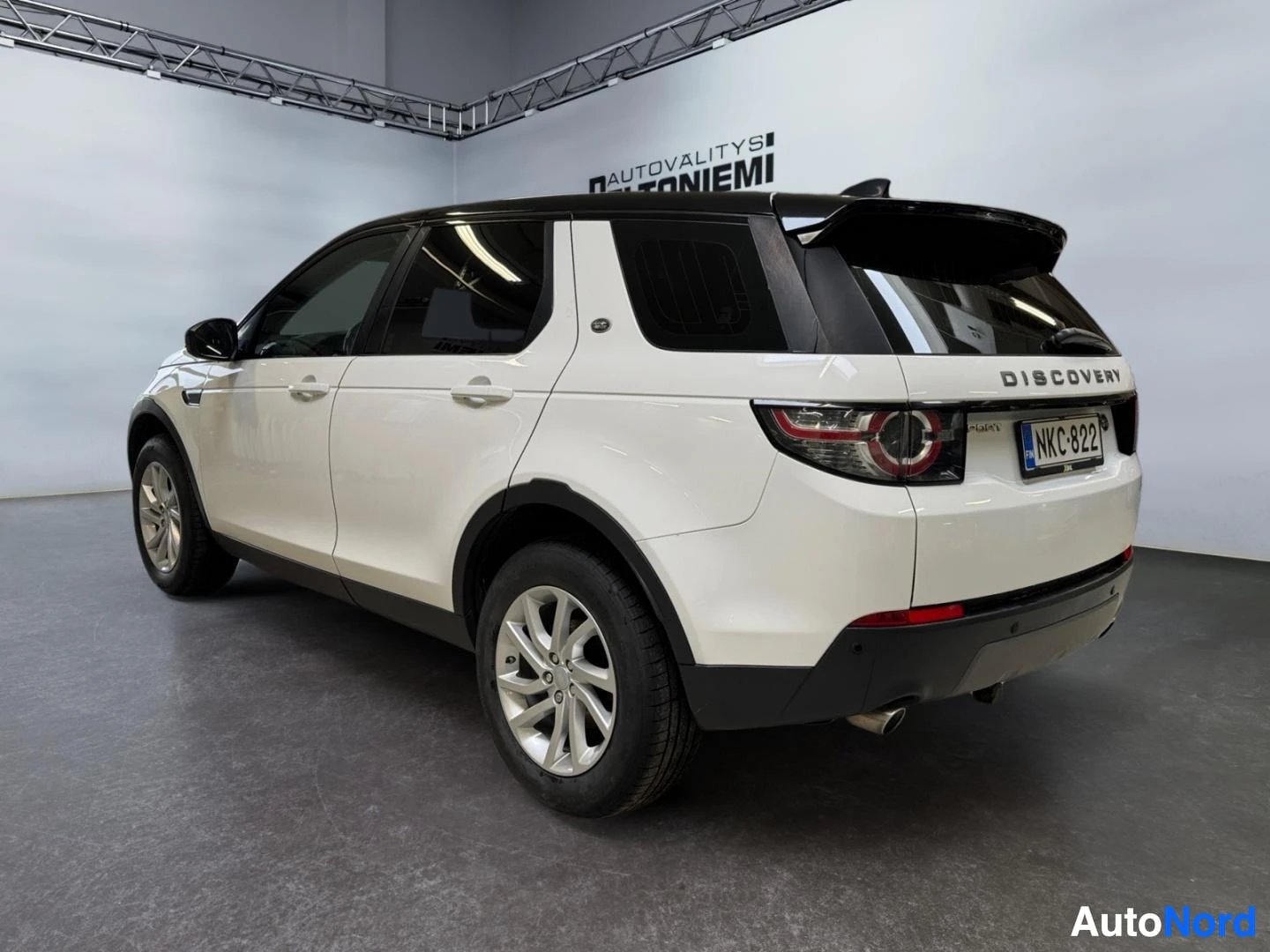 Takaviisto: Land Rover Discovery Sport, takakulmakuva valkoisesta autosta mustalla katolla sisätiloissa.