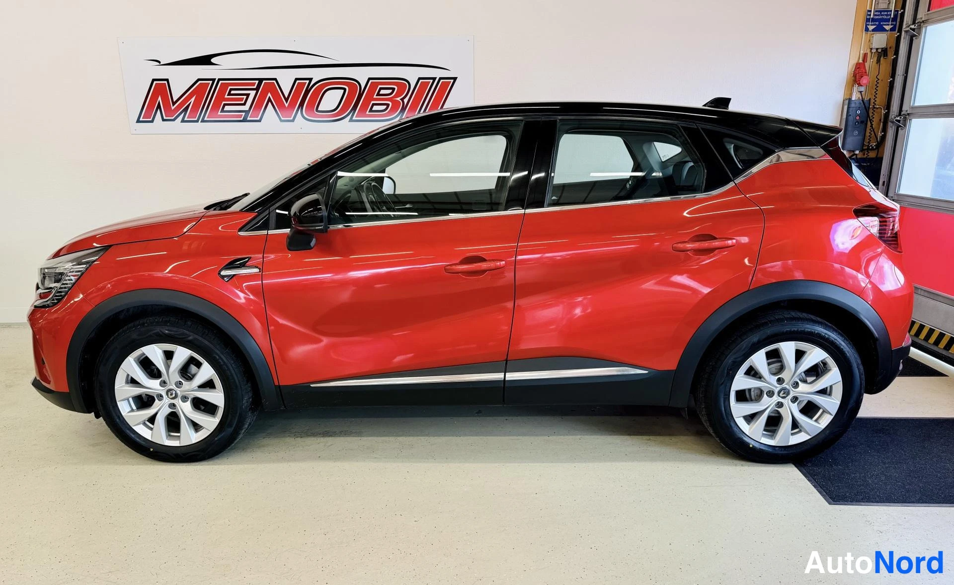 Sivulta: Punainen Renault Captur etukulmasta sisätiloissa MENOBIL-logon edessä.