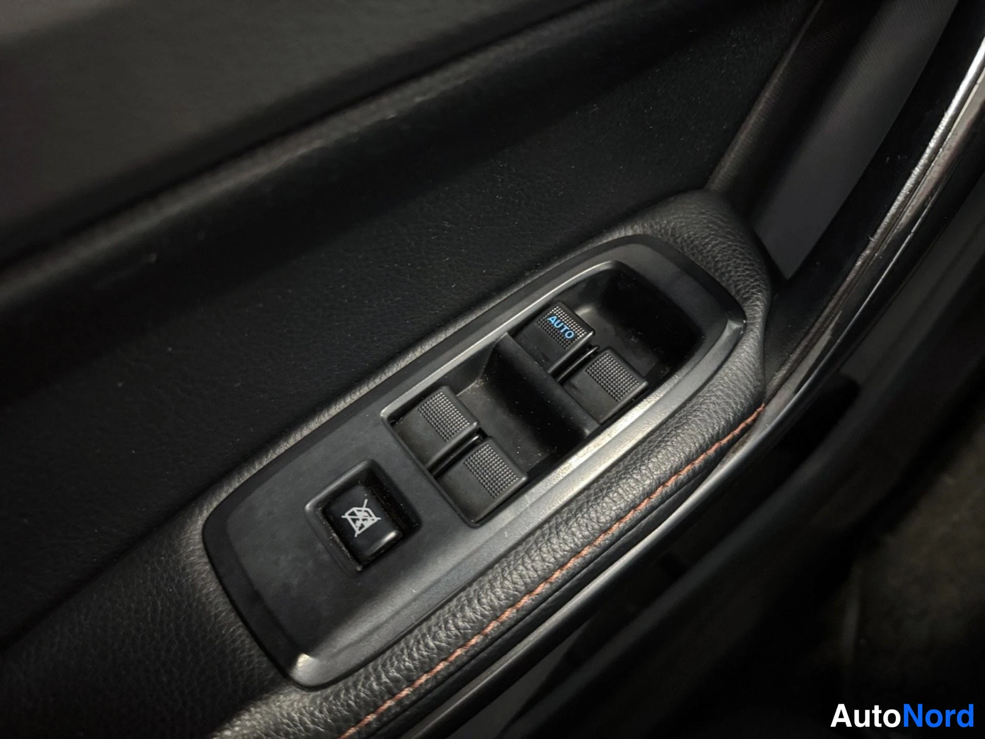 Yksityiskohta: Oven sisäpaneelin sähköikkunanokytkimet, yksi AUTO-merkitty; oranssit ompeleet mustassa nahassa.