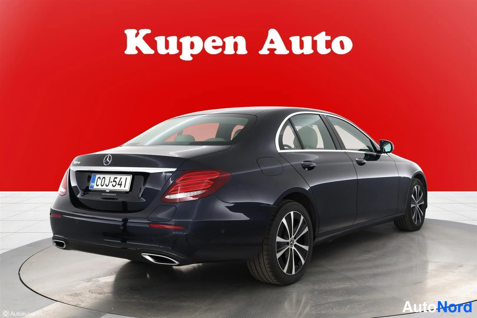 Takaviisto: Mercedes-Benz E -sedan takaa kolmannesta vinkkelistä, tummansininen koripinta, kokonainen auto kuvassa.
