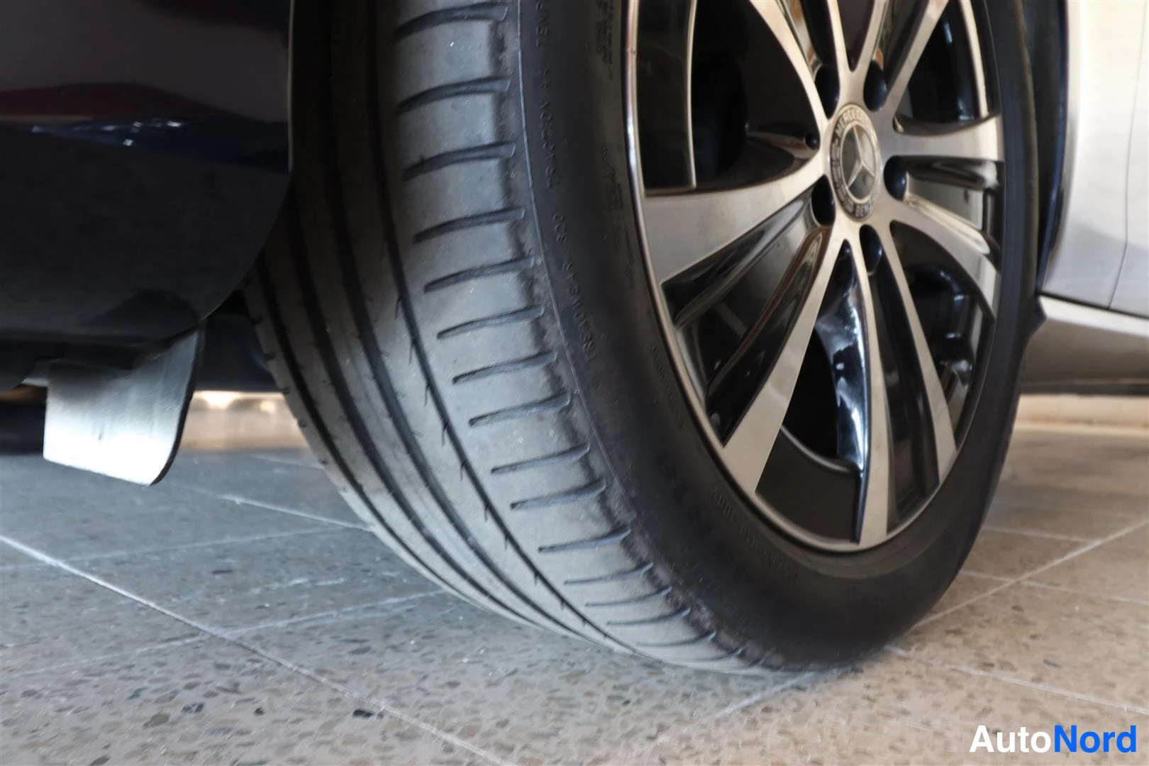 Yksityiskohta: Lähikuva auton takarenkaasta ja hopea-mustasta Mercedes-tähdellä varustetusta alumiinivanteesta, liit Shift:ki lpollisella päiv; aut portaid...