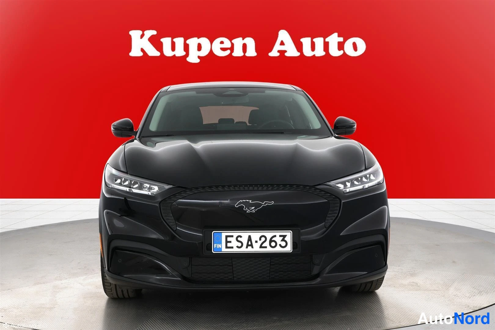 Edestä: Musta Ford Mustang Mach-E suoraan edestä, rekisteritunnus, punainen tausta