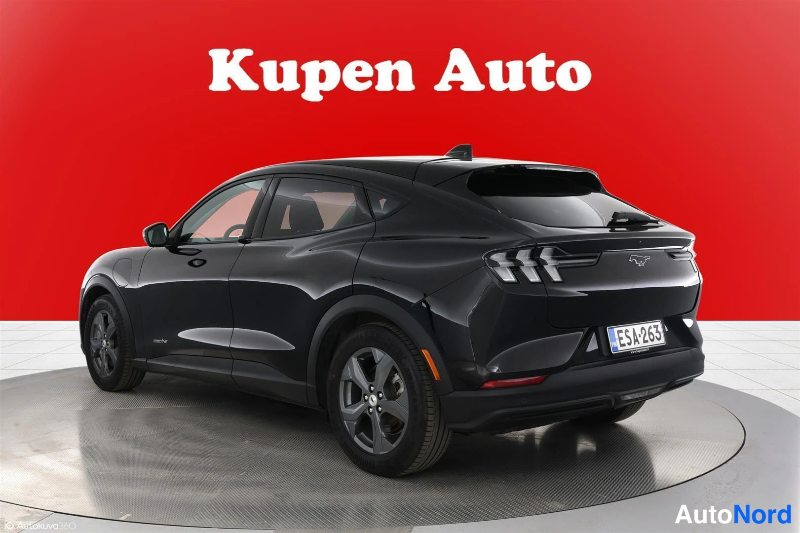 Takaviisto: Musta Ford Mustang Mach-E takakulmasta vasemmalta kuvattuna, rekisteritunnus punaisella taustalla.