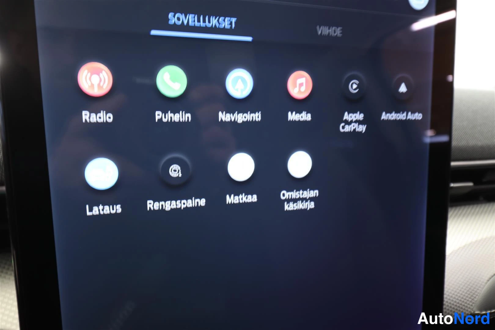 Yksityiskohta: Infotainment-näytön sovellusvalikko: Radio, Puhelin, Navigointi, Media, Apple CarPlay, Android Auto, Lataus, Rengaspaine, Matkaa, Omistajan käsikirja.