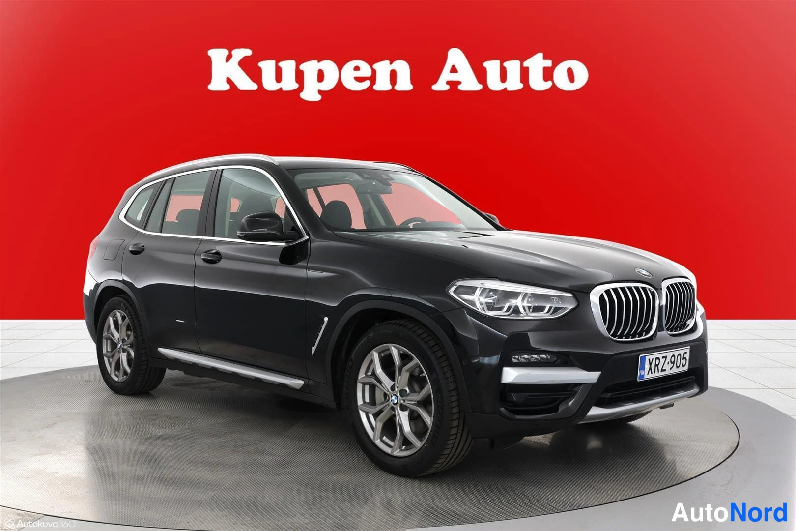Etuviisto, nokka oikealle: Musta BMW X3 -maasturi punaisella taustalla, kolmen kvartaalin etukuva vasemmalta, hopeavanteet.