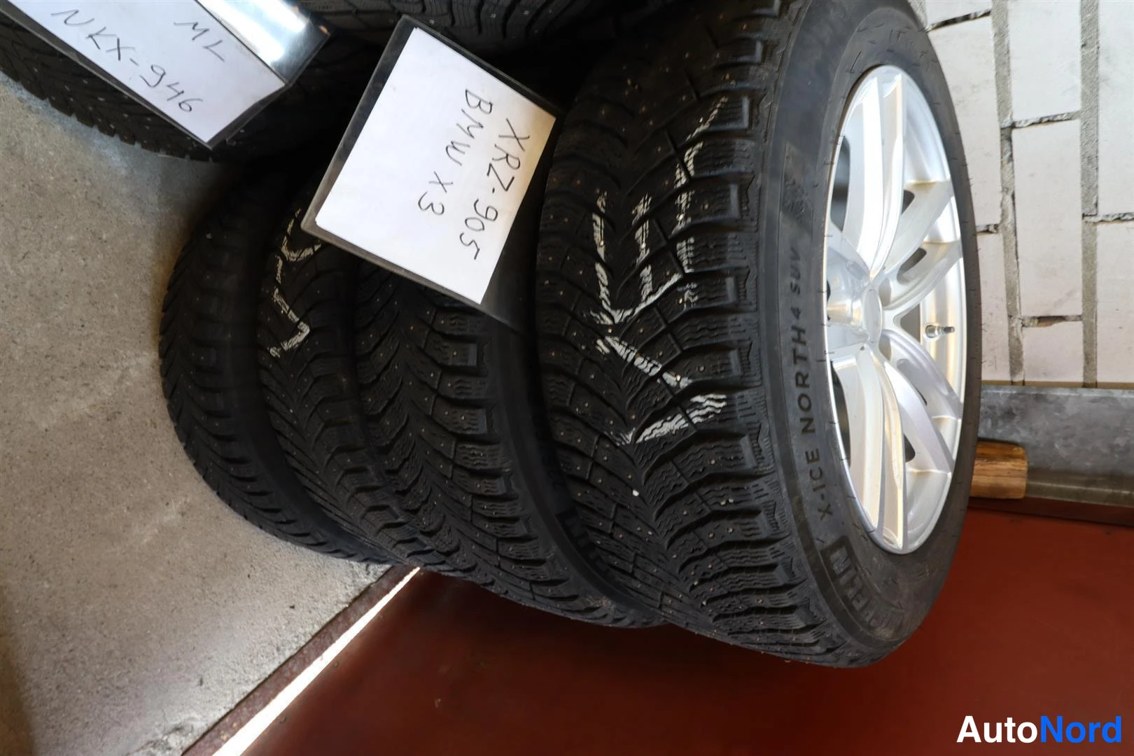 Yksityiskohta: Pinossa neljä talvirenkasta alumiinivanteilla, kyltillissä lukee ' BMW X3'.