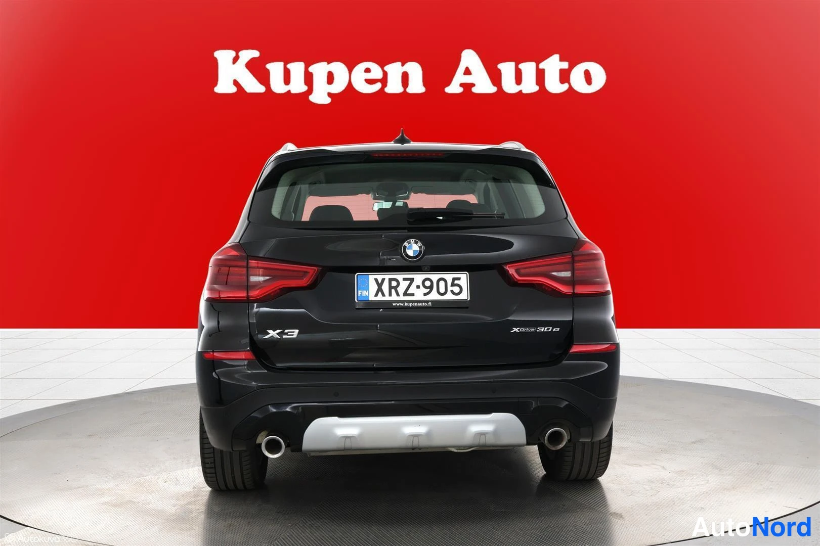 Takaa: Musta BMW X3:n perä suoraan takaa kuvattuna, rekisterikilpi, punainen tausta.