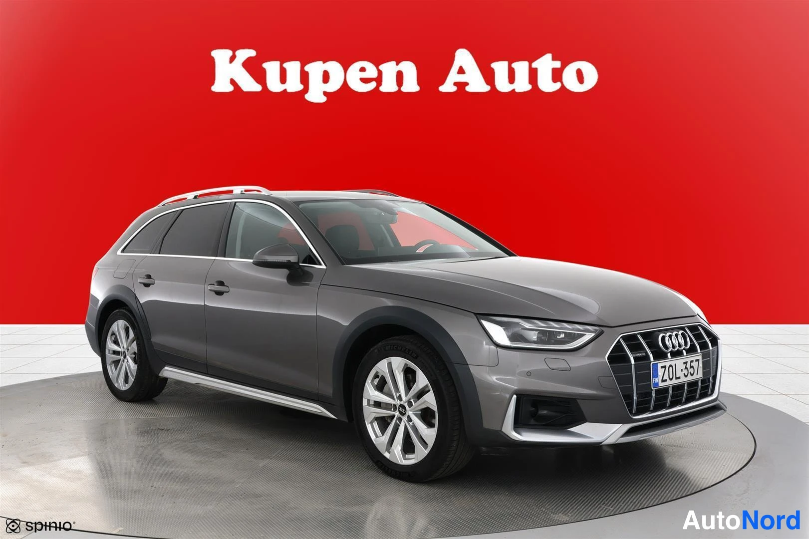 Etuviisto, nokka oikealle: Harmaa Audi A4 Allroad -farmari punaisella taustalla, kolmen neljännesetuvasento, kattokaiteet ja alumiinivanteet näkyvissä.