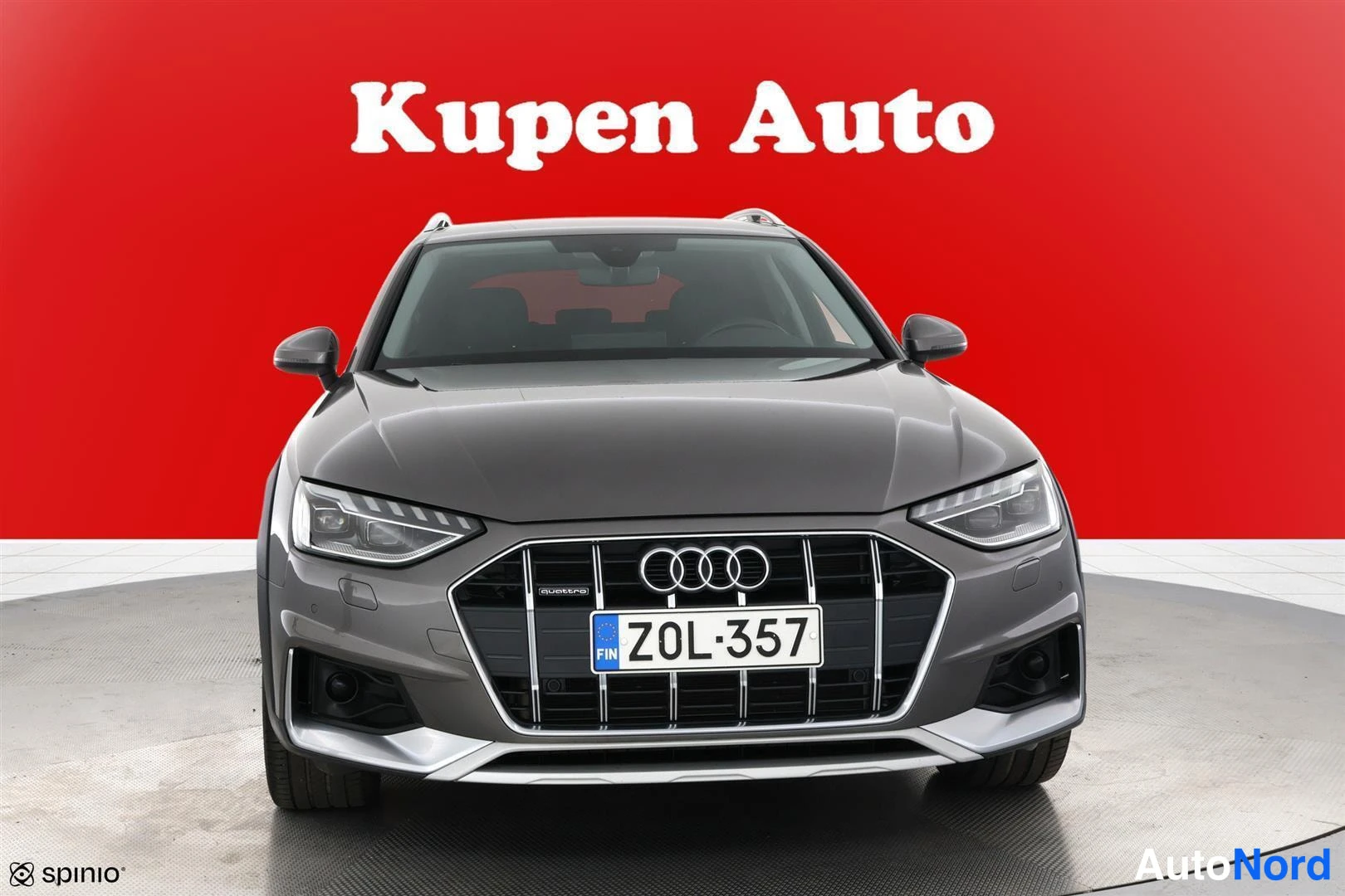 Edestä: Harmaan Audi A4 Allroadin etunäkymä suoraan edestä punaisella taustalla, A4-kori ja rekisteritunnus.