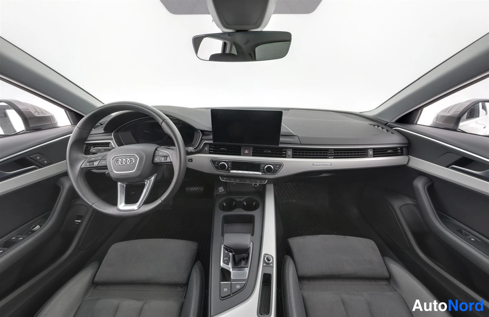 Muu: Sisätilakuva etupäältä: Audi-ohjauspyörä, kojelauta ja irrallinen keskinäyttö, tummat istuimet.