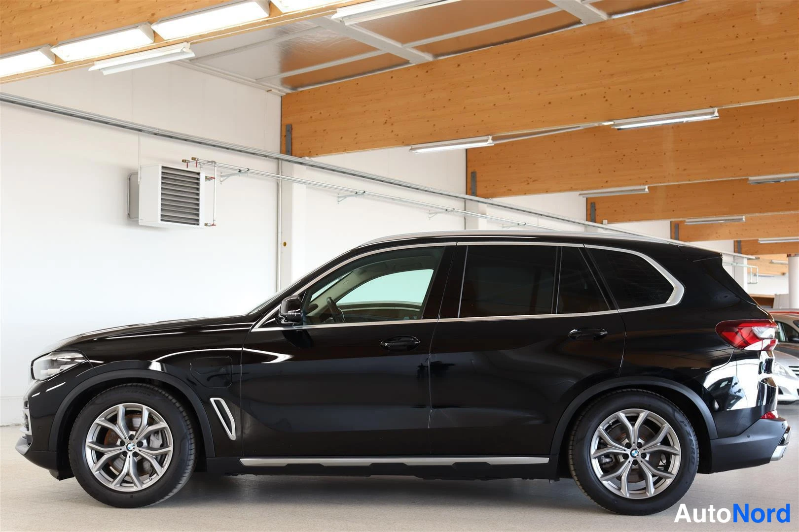 Etuviisto, nokka vasemmalle: Mustan BMW X5:n sivuprofiili vasemmalta sisätiloissa, kevytmetallivanteet ja kromilistat.