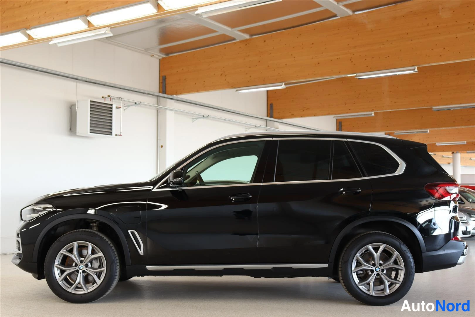 Sivulta: Musta BMW X5 sivulta sisähallissa, tummat ikkunat ja kevytmetallivanteet.