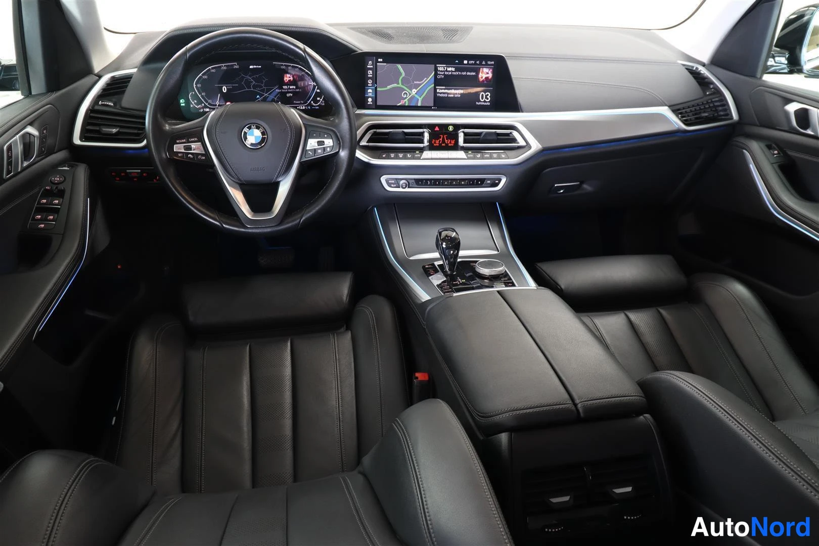 Ohjaamo: Ohjaamo edestä: BMW-ohjauspyörä, digitaalinen mittaristo, keskikonsolin näyttö ja mustat nahkapenkit.