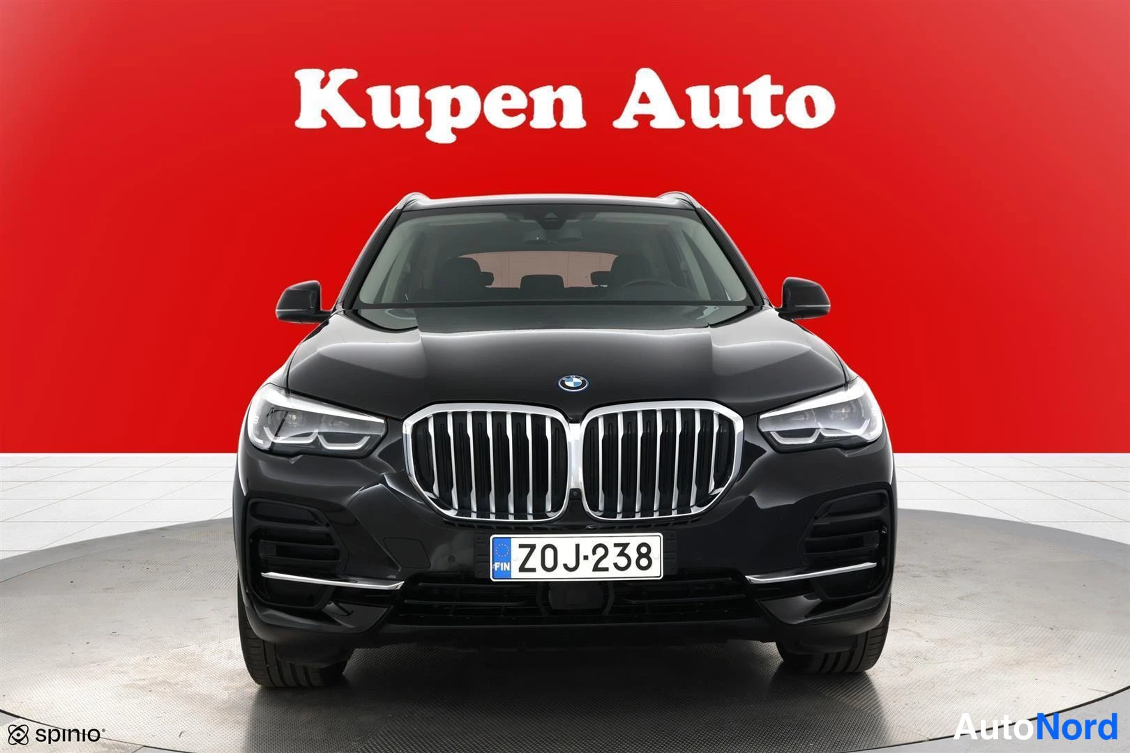 Edestä: BMW X5, tummanmusta, suora etukuva punaisella taustalla.