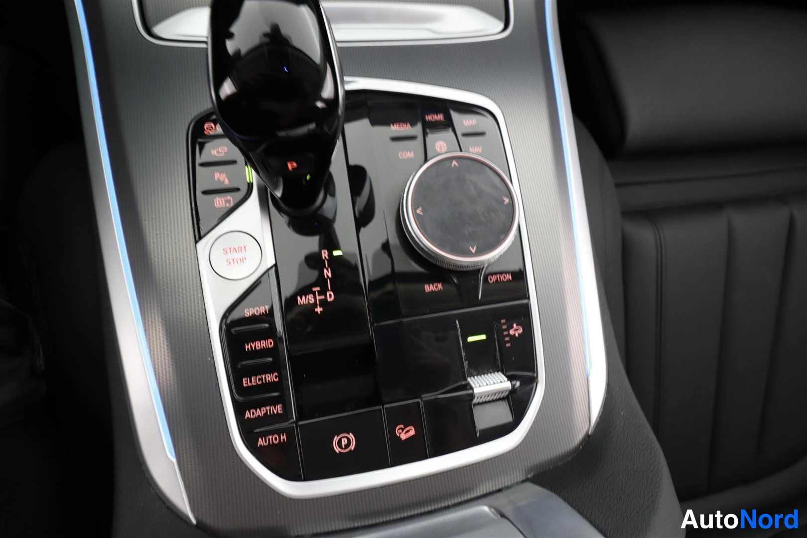 Yksityiskohta: Auton keskikonsolin näkymä: automaattivaihteen valitsin, iDrive-ohjainnuppi, START STOP -painike ja ajotilapainikkeet SPORT, HYBRID, ELECTRIC, ADAPTIVE ja AUTO