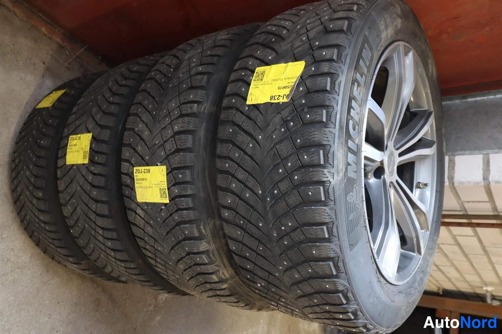 Yksityiskohta: Neljä nastarengasta alumiinvanteilla pinossa; Michelin-merkintä näkyvissä, keltaisia tunnisteita