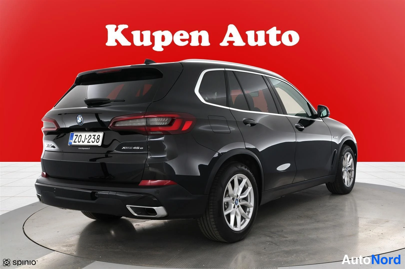 Takaviisto: Mustan BMW X5:n takakulman kuva punaisella taustalla, rekisterikilpi.