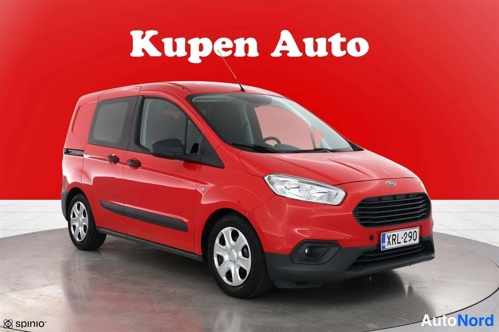 Etuviisto, nokka oikealle: Punainen Ford Transit Courier pakettiauto etuviistosta oikealta, rekisteri, valkoviistreillä vanteilla.