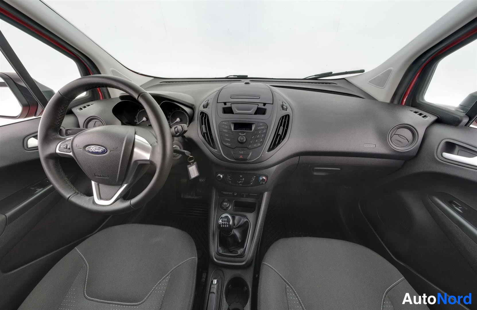 Ohjaamo: Ohjaamo edestä: Ford-ohjauspyörä, manuaalivaihteisto, kankaanpenkit ja keskikonsoli, tummat sisäpanelit.