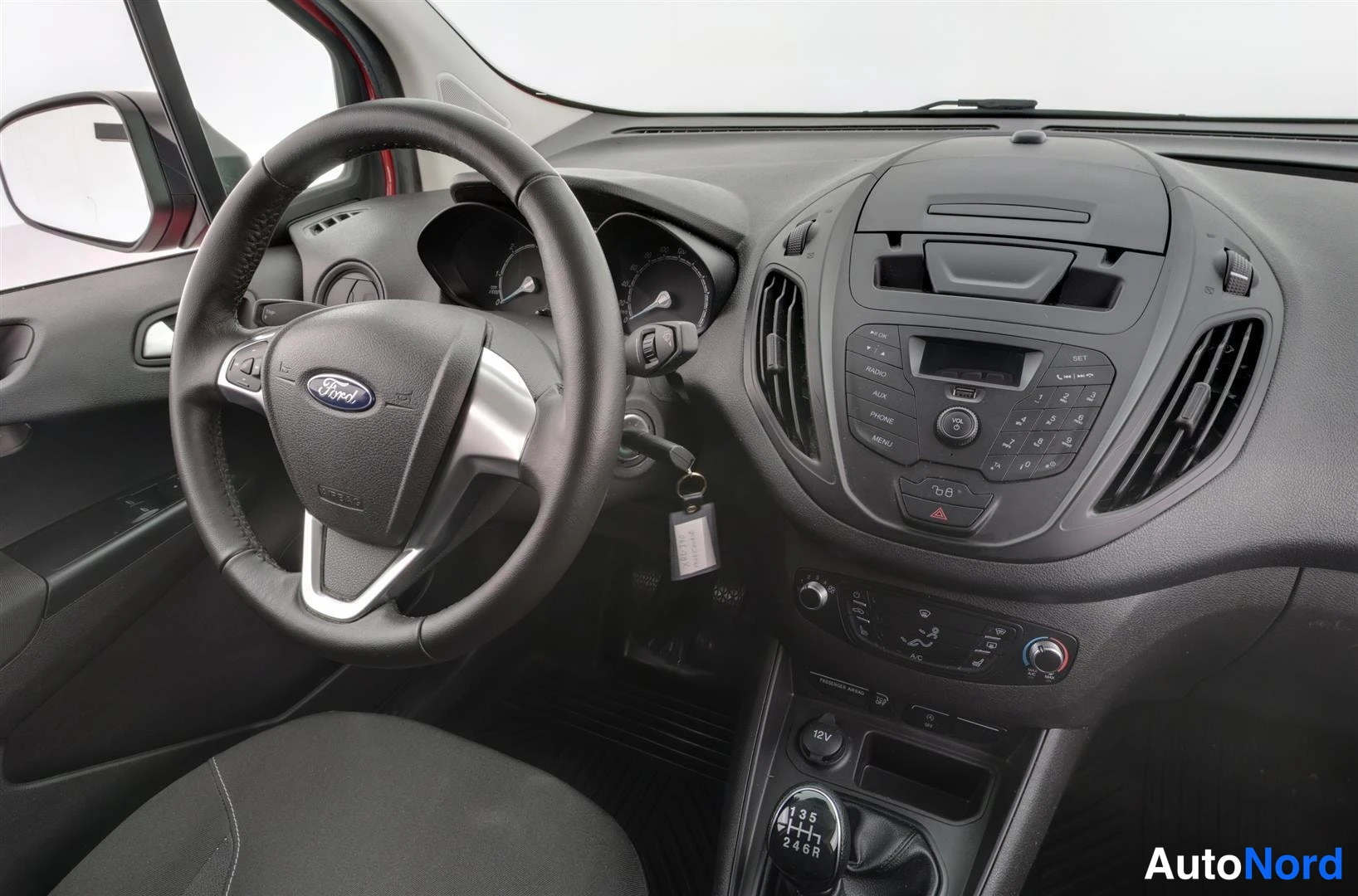 Ohjaamo: Lähikuva ohjaamosta: Ford-ohjauspyörä monitoiminäppäimillä, radiopaneeli ja manuaalivaihteen keppi.