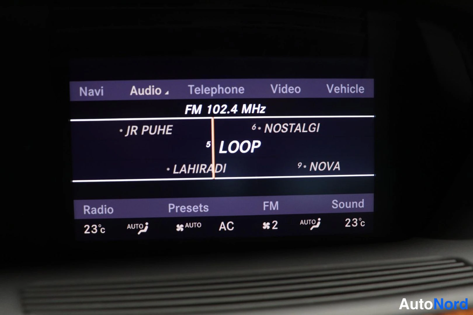 Yksityiskohta: Auton infotainment-näyttö radionäkymässä, FM 102.4 MHz, valikot Navi, Audio, Telephone, Video, Vehicle.