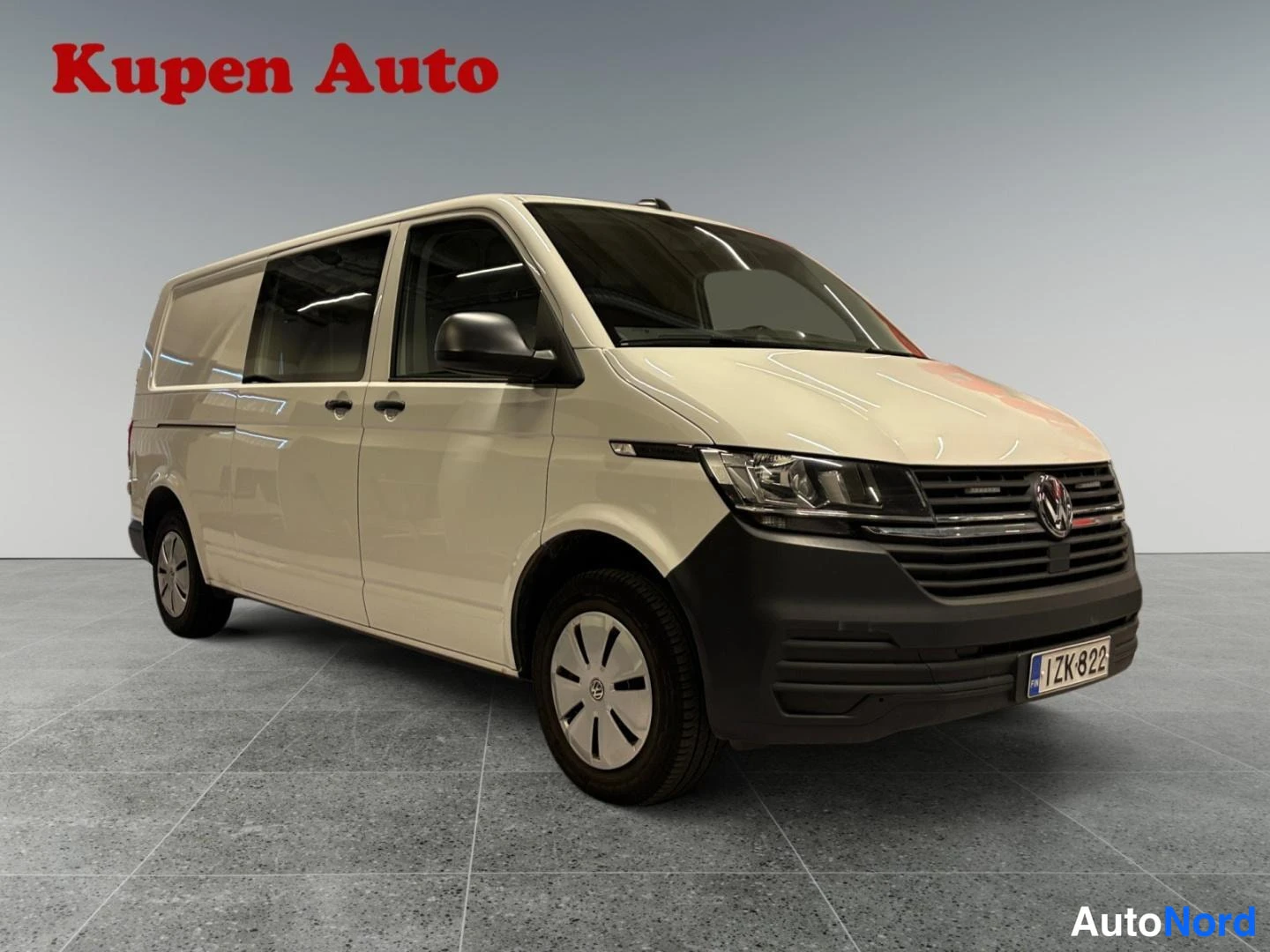 Etuviisto, nokka oikealle: Valkoinen Volkswagen Transporter -pakettiauto kulmakuva edestä oikealta, pitkä akseliväli ja takaovi.
