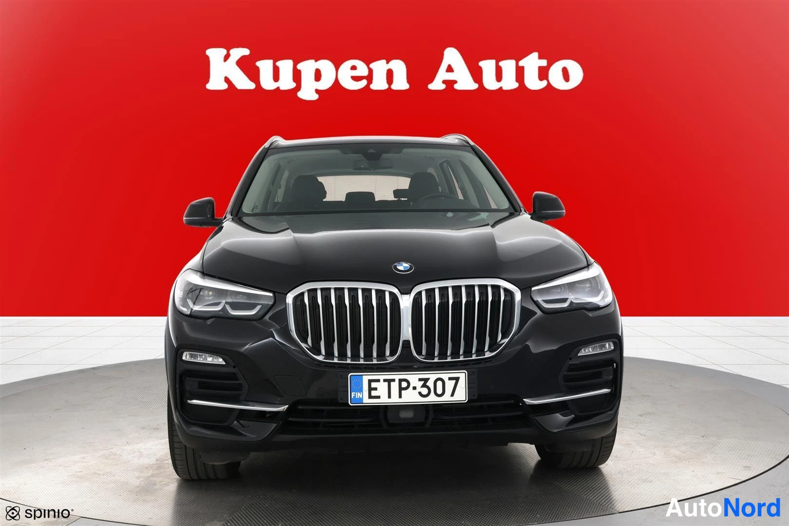 Edestä: BMW X5 suoraan edestä päin kuvattuna, etusäleikkö ja ajovalot näkyvät, punainen tausta.